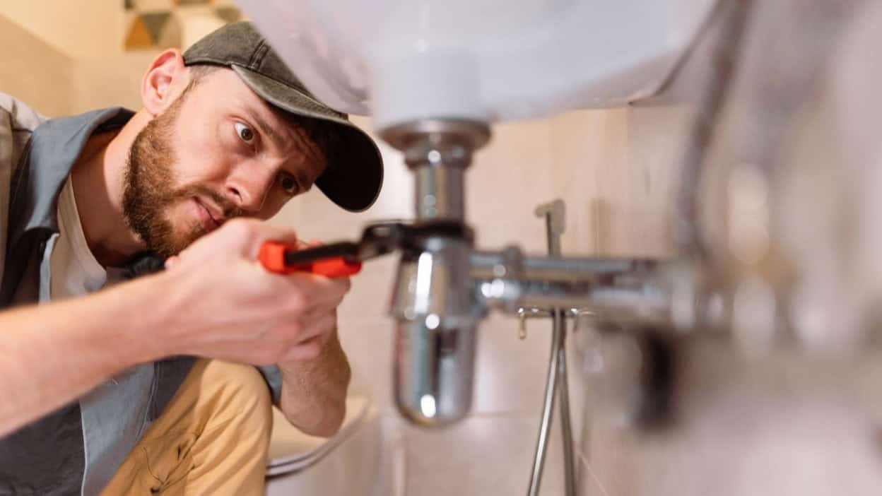 London plumber fixing a burst pipe under sink during emergency water leak repair