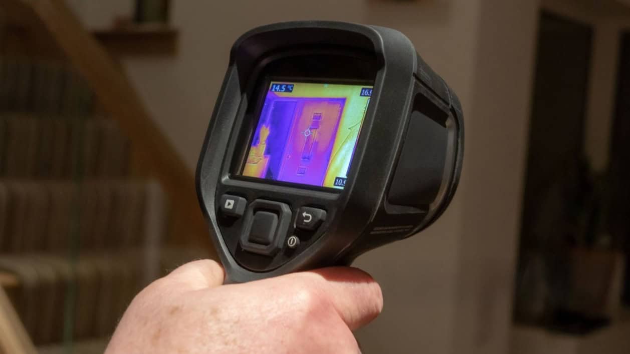 Plumber using thermal imaging camera to find hidden leak behind wall in London home